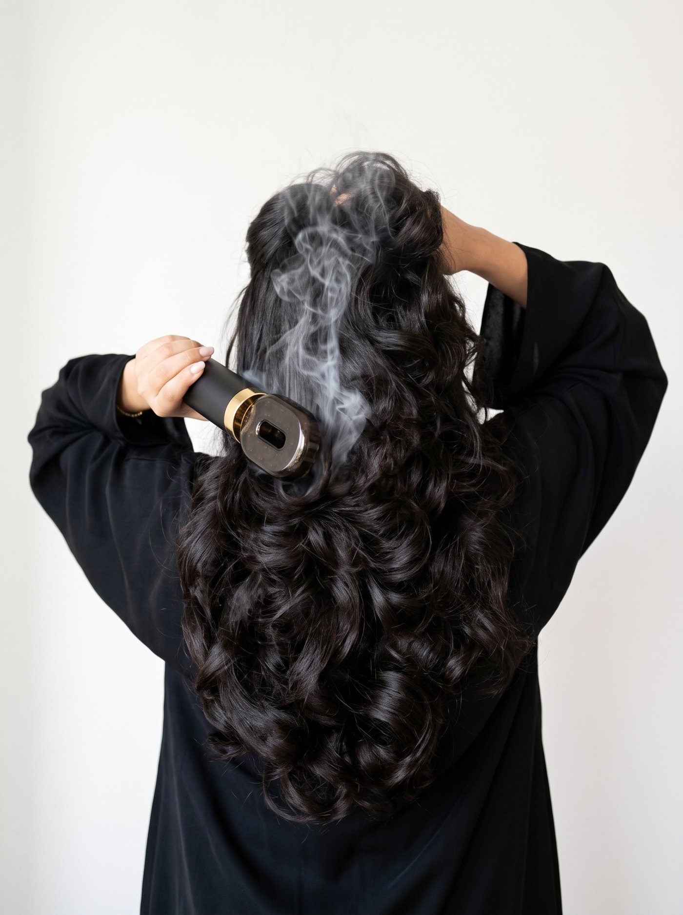 Woman in a black abaya brushing bakhoor smoke through her hair
