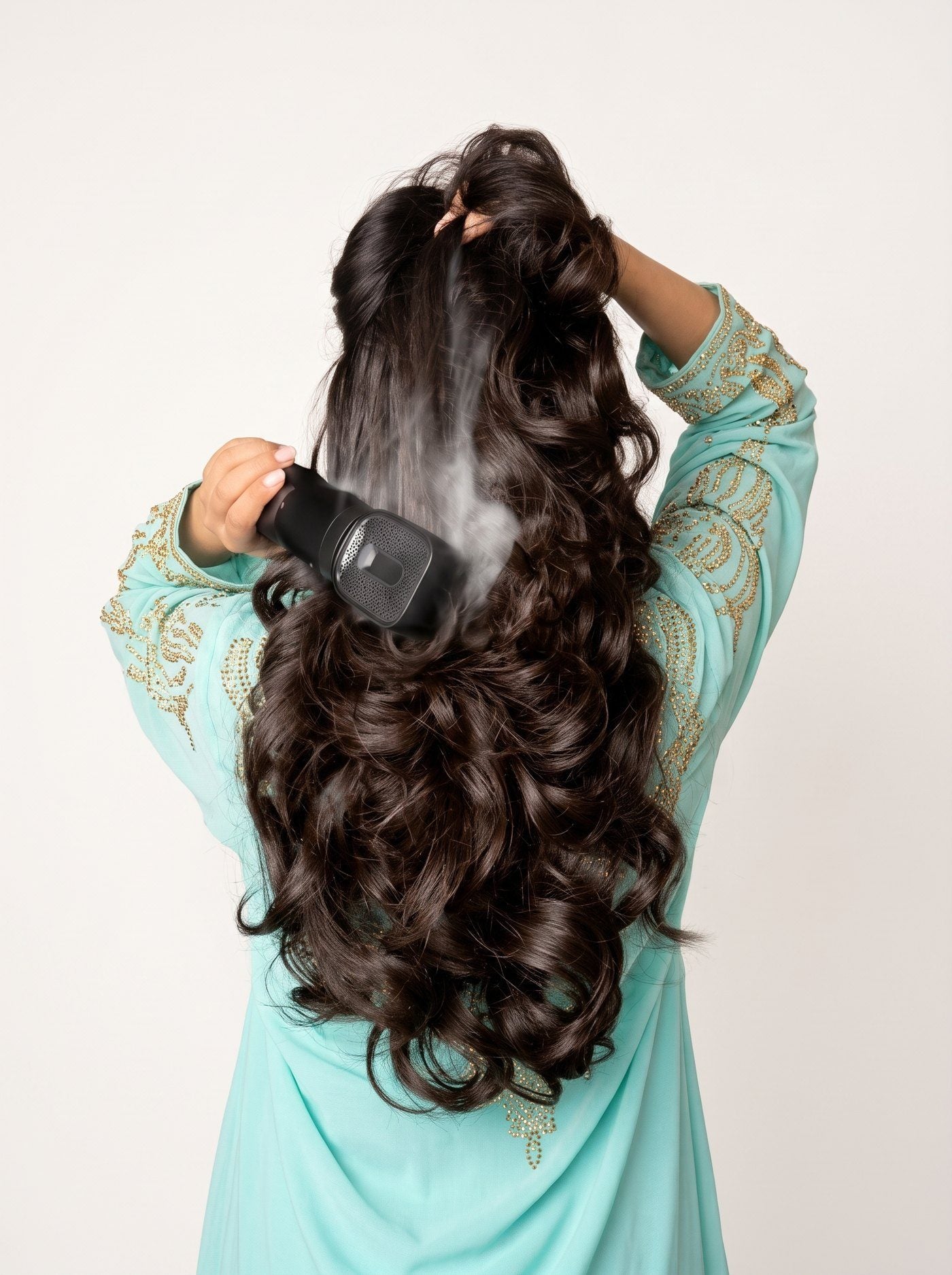 Woman in a turquoise kaftan brushing bakhoor through her hair