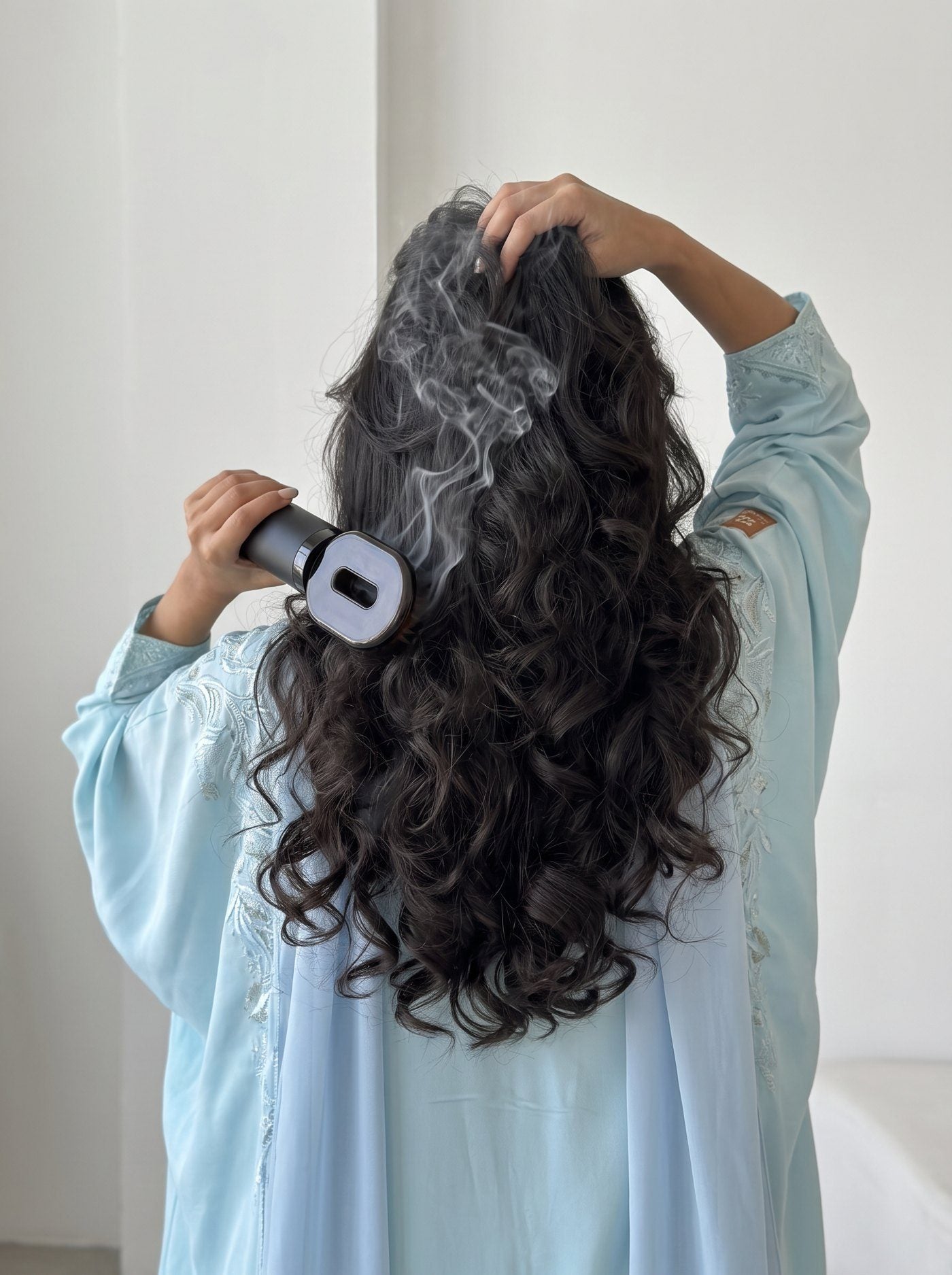 Woman in a light blue abaya brushing bakhoor through her hair